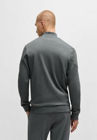 Felpa grigia con collo alto, maniche lunghe e polsini a costine. Tessuto liscio e vestibilità comoda, abbinata a joggers grigi coordinati.