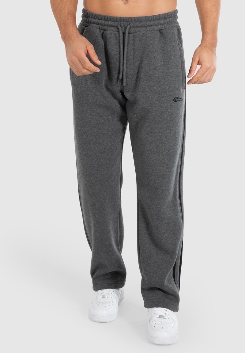 Graue Sweatpants mit einem Kordelzugbund, geraden Beinen und einem dezenten Logo-Detail. Kombiniert mit weißen Sneakers.