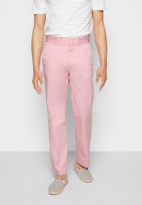 Ljusrosa byxor med rak benform, knäppning och sidofickor, tillverkade av ett slätt tyg. I kombination med grårandiga slip-ons.