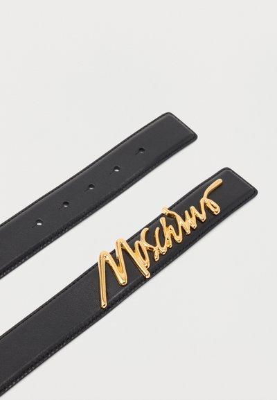 Ceinture en cuir noir avec boucle dorée en forme de lettres scriptes épelant un nom de marque, dotée de plusieurs trous de réglage sur un fond clair.