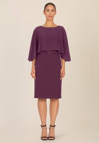 Violet mekko, jossa on virtaava viittamainen ylisuoja, joka korostaa vartalon muotoja ja jossa on pitsikoristeet vyötäröllä. Sujuvaa kangasta, polvenpituinen muotoilu.