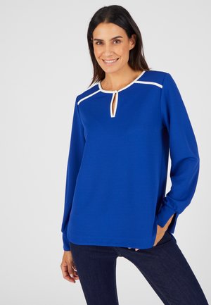 Top de manga larga azul royal con escote en forma de ojal, detalles en blanco, corte relajado y aberturas laterales en el dobladillo para un toque adicional.