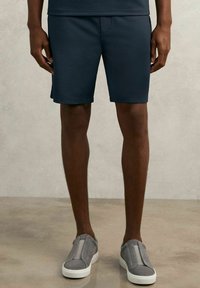 Marineblaue Shorts aus strukturiertem Stoff, mit elastischem Bund und modernem Schnitt, kombiniert mit grauen Slippers.
