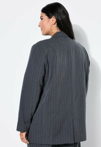 Harmaa raidoitettu bleiseri, jossa on istuva leikkaus, pitkät hihat, yksittäinen halkio ja tekstuuri. Huomionarvoinen klassisesta suunnittelustaan ja rakenteestaan.