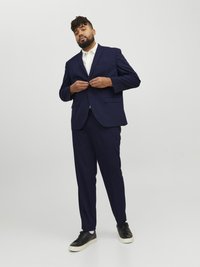 Navy blue suit with a single-breasted jacket and matching trousers, paired with a white shirt and black sneakers. Smooth fabric, tailored fit.