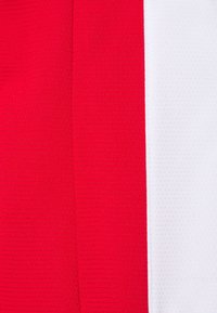 Deux panneaux de tissu verticaux, l'un rouge vif à gauche et l'autre blanc à droite, avec des coutures texturées visibles.