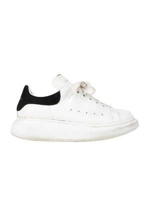 Baskets blanches avec semelle épaisse et languette noire au talon, avec des lacets blancs et de petits trous de ventilation sur le côté.
