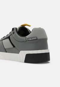 Gray sneaker with a textured upper, featuring a yellow pull tab, black accents, and a white rubber sole with a ridged design.