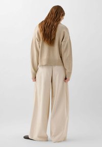 Beige gebreide trui met een cropped ontwerp, geribbelde zoom en lange mouwen, gecombineerd met brede beige broeken, die een gladde textuur tonen.