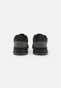 Black athletic shoes with gray suede accents. Textured fabric upper, padded collar, and rubber sole. Features logo on heel and patterned laces.