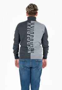 Maglione bloccato nei colori grigio e grigio scuro con colletto alto, caratterizzato da un audace design testuale sulla parte posteriore. Indossato con jeans blu.