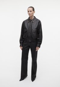 Zwarte leren cropped jasje met twee voorkeurszakken, contrasterende stiksels en een elastische tailleband, gecombineerd met strakke zwarte leren broek.