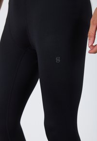 Fekete sportleggings rugalmas anyagból, sima textúrával. Kicsi logóval a combon. A kényelem és a mozgás szabadsága érdekében készült.
