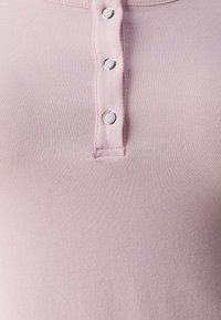 Svijetloružičasti pamučni henley top s zatvaranjem na tri gumba, glatkom teksturom i rebrastim materijalom. Pogodan za svakodnevno nošenje.