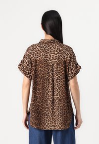 Skjorta i leopardmönster i lättviktsmaterial med uppkavlade ärmar, krage och sidslitsar. Har en avslappnad passform och en färgpalett i brunt och tan.