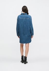 Farkkupaitamekko, jossa sininen kuviointi, kauluksellinen pääntie, pitkät hihat ja sivuhalkiot, yhdistetty mustiin nilkkureihin.