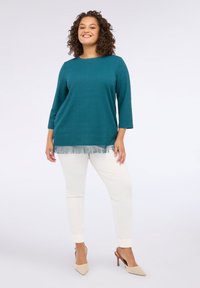 Top texturat teal cu mâneci 3/4, având un tiv franjurat; asortat cu pantaloni crem slim și pantofi cu vârf ascuțit de un bej deschis.