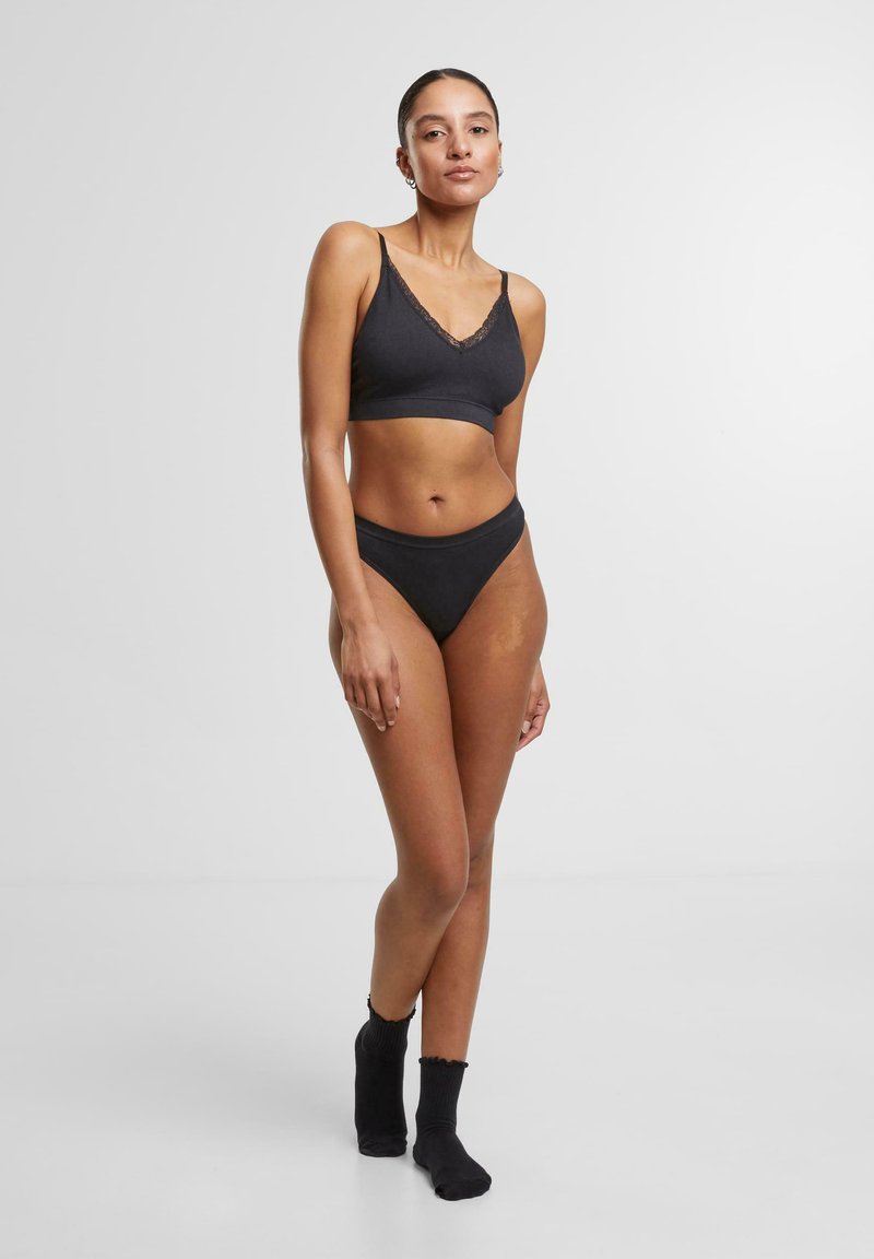 Black cotton bralette with lace trim and matching high-waisted briefs, featuring a smooth texture and adjustable straps. Black crew socks included.