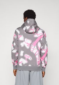 Mand i grå hættetrøje med hvid og pink abstrakt spraymønster, set fra ryggen, parret med lys grå shorts.