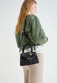Borsa a mano in pelle nera con una forma strutturata, manico intrecciato, dettagli in metallo dorato e chiusura a pattina angolare. Inclusa tracolla.