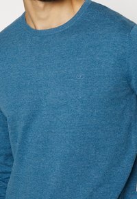 Blauer gestrickter Pullover mit Rundhalsausschnitt und langen Ärmeln. Verfügt über ein dezentes Logo auf der Brust und gerippte Bündchen für mehr Textur.