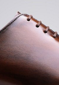 Chaussure en cuir brun avec une texture lisse, bout arrondi, couture décorative et six œillets pour les lacets le long du bord supérieur.