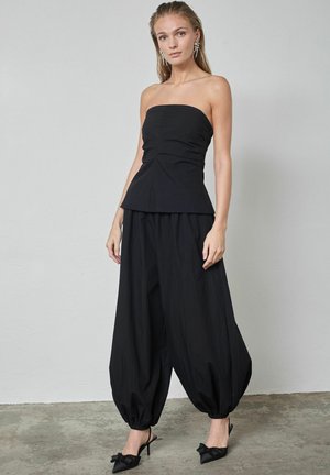 Must mustuta top, millel on keha vormiv osa ja peplum-detail, kombineeritud lahtiste, voltidega mustade pükstega ning mustade kontsadega slingback-kingadega, millel on detailid.