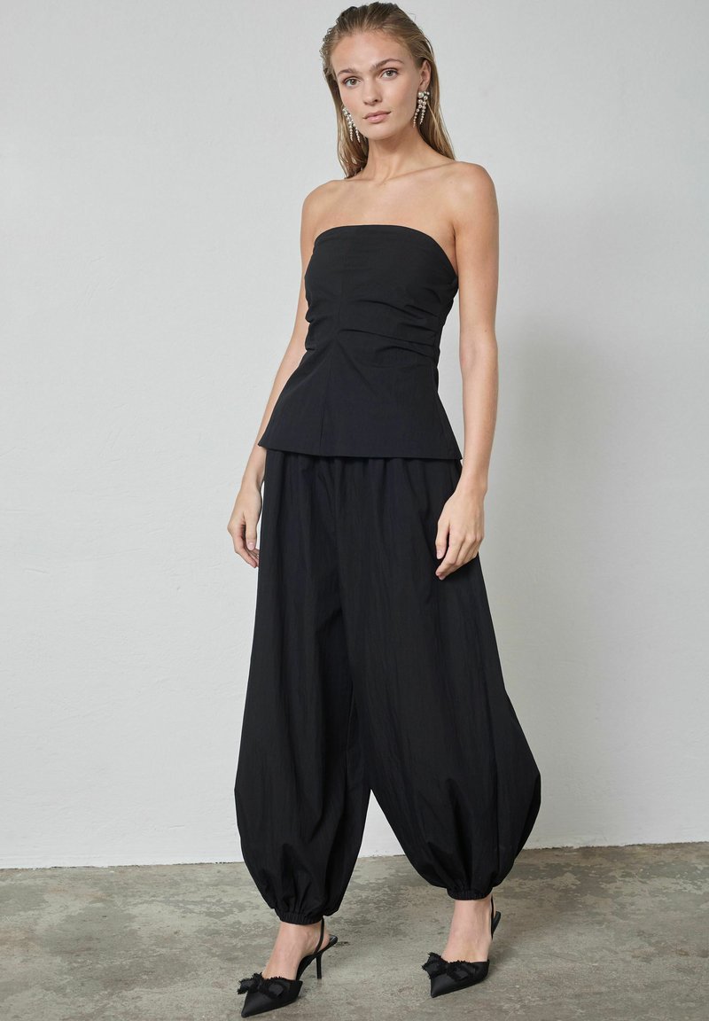 Zwarte strapless top met een aangesloten lijfje en peplumdetail, gecombineerd met losse, gedrapeerde zwarte broek en zwarte slingback hakken met accenten.