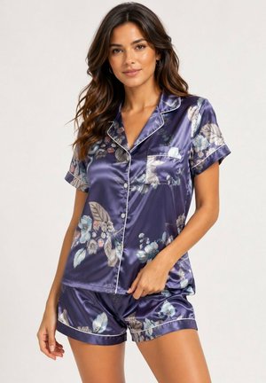 Femme portant un haut de pyjama en satin floral violet foncé brillant à manches courtes et un short assorti sur un fond uni.