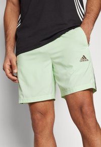 Ljusgröna träningsshorts i ett ventilerande tyg, med resårmidja och en gul logotyp längst ner till vänster.