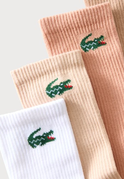 Trois chaussettes côtelées en blanc, beige et marron clair avec un logo crocodile vert brodé près du haut.