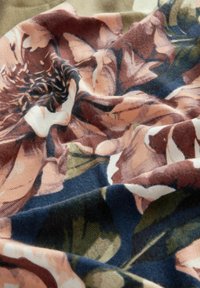 Tessuto floreale con grandi fiori rosa e crema morbidi, accompagnati da foglie verdi su uno sfondo blu scuro. La texture sembra liscia e lussuosa.