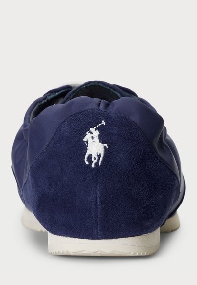 Temno modni čevlji, izdelani iz usnja in sintetičnih materialov, z teksturirano zadnjo stranjo, elastičnim robom in belim logotipom konjarja.