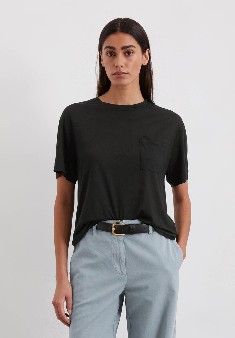 Zwart T-shirt met korte mouwen en een ronde hals, met een borstzak, gecombineerd met lichtblauwe broek en een zwarte riem met een gouden gesp.