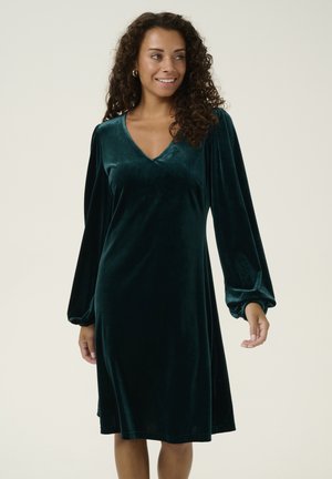 Robe en velours vert avec un décolleté en V et de longues manches ballons. Le design longueur genou présente une coupe décontractée et un léger éclat.