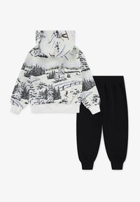 Hooded dukserica u bijeloj boji s printom zimskog krajolika i crnim treniranim hlačama. Outfit sadrži elastične manžete i opušteni kroj.