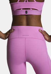 Jasnoróżowe legginsy sportowe z wysokim stanem, z przeszyciem i etykietą "SWISS ENGINEERING" z tyłu.