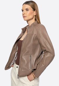 Braune Lederjacke mit Stehkragen, Reißverschluss vorne und Seitentaschen. Glatte Textur mit Nähten und Reißverschlüssen.