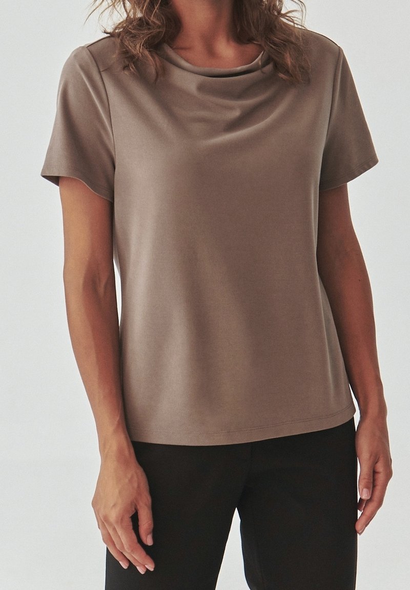 T-shirt a maniche corte color bronzo con scollatura drappeggiata, texture liscia e vestibilità rilassata, abbinato a pantaloni neri.