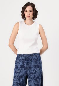 Haut sans manches blanc avec un col rond, associé à un pantalon bleu à motifs avec une taille élastique et des poches latérales.
