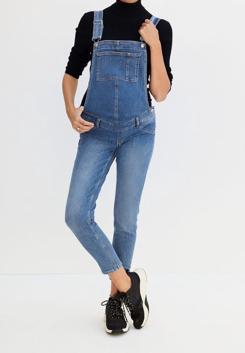 Denim overalls with adjustable straps, front pocket, and tapered legs. Worn over a black turtleneck, paired with black sneakers.