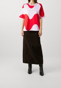 Camiseta de manga corta, de color blanco y rojo con un patrón ondulado, combinada con una falda larga de mezclilla negra y botas negras de tobillo. Tela suave, diseño casual.