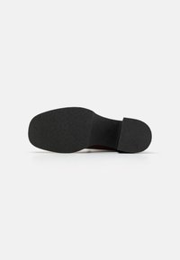Suela de zapato de goma negra con superficie de agarre texturizada, área de puntera ancha y ligera elevación en el arco. Sin marcas ni patrones visibles. Diseño de tacón redondeado.