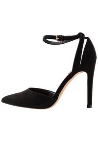 Černá semišová vysoká podpatková bota s špičatou špičkou, kotníkovým páskem se zlatou sponou a elegantním jehlovým podpatkem. Hladká textura a minimalistický design.