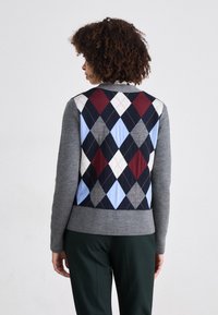 Grå genser med et fargerikt argyle-mønster i rød, blå og svart på baksiden, med en tettsittende design og ribbet kant.