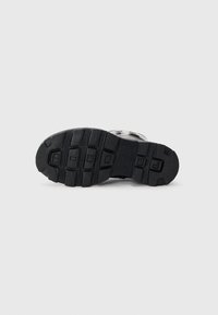 Black rubber outsole with textured grip pattern, featuring sturdy treads and raised letters. Smooth edges and solid construction.