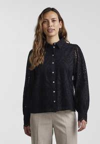 Black shirt with intricate cut-out pattern, long sleeves with gathered cuffs, and a button-down front. Lightweight fabric with a textured finish.