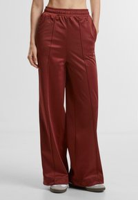 Wide-leg pants in a deep burgundy color, featuring an elastic waistband, side pockets, smooth texture, and subtle vertical seam accents.