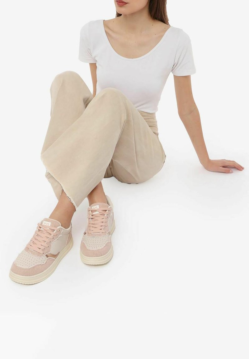 Zapatillas de deporte rosa claro con detalles de ante y malla, que presentan una puntera perforada y suela de goma de color crema, llevadas con pantalones beige.