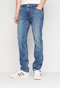 Jeans din denim de culoare albastru deschis, cu o croială dreaptă, cinci buzunare și închidere cu nasture. Asortate cu adidași albi cu dungi gri.